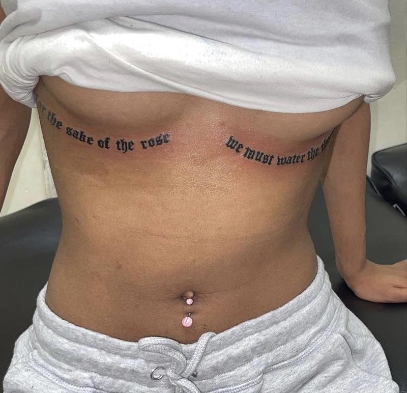 Old English script lettering tattoo across the stomach