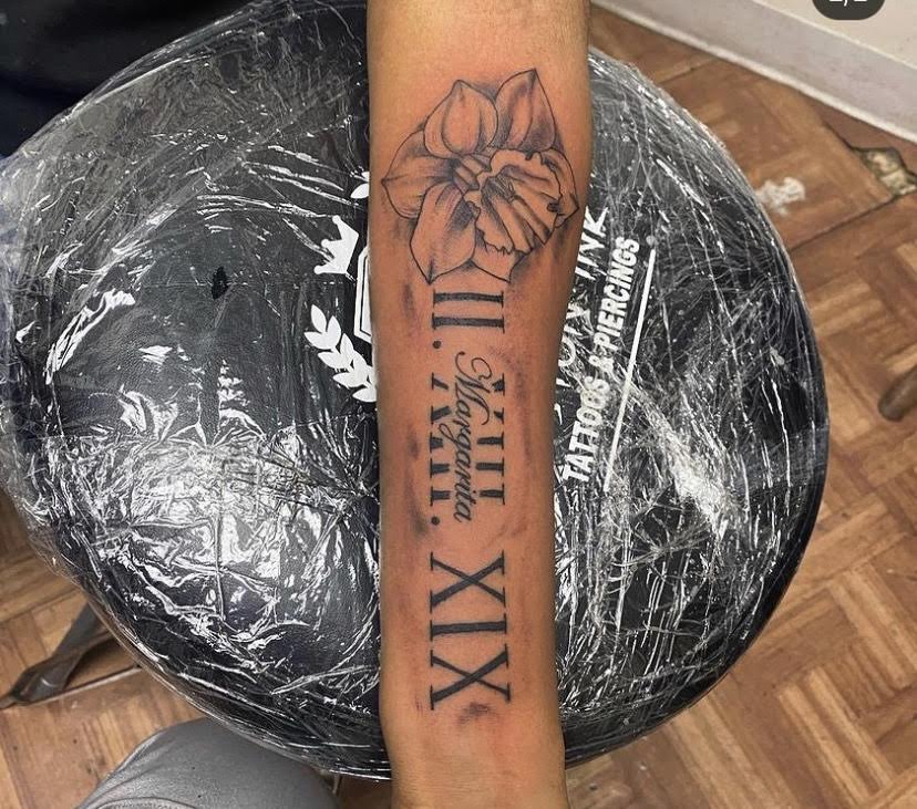 Daffodil and Roman numeral tattoo on the forearm