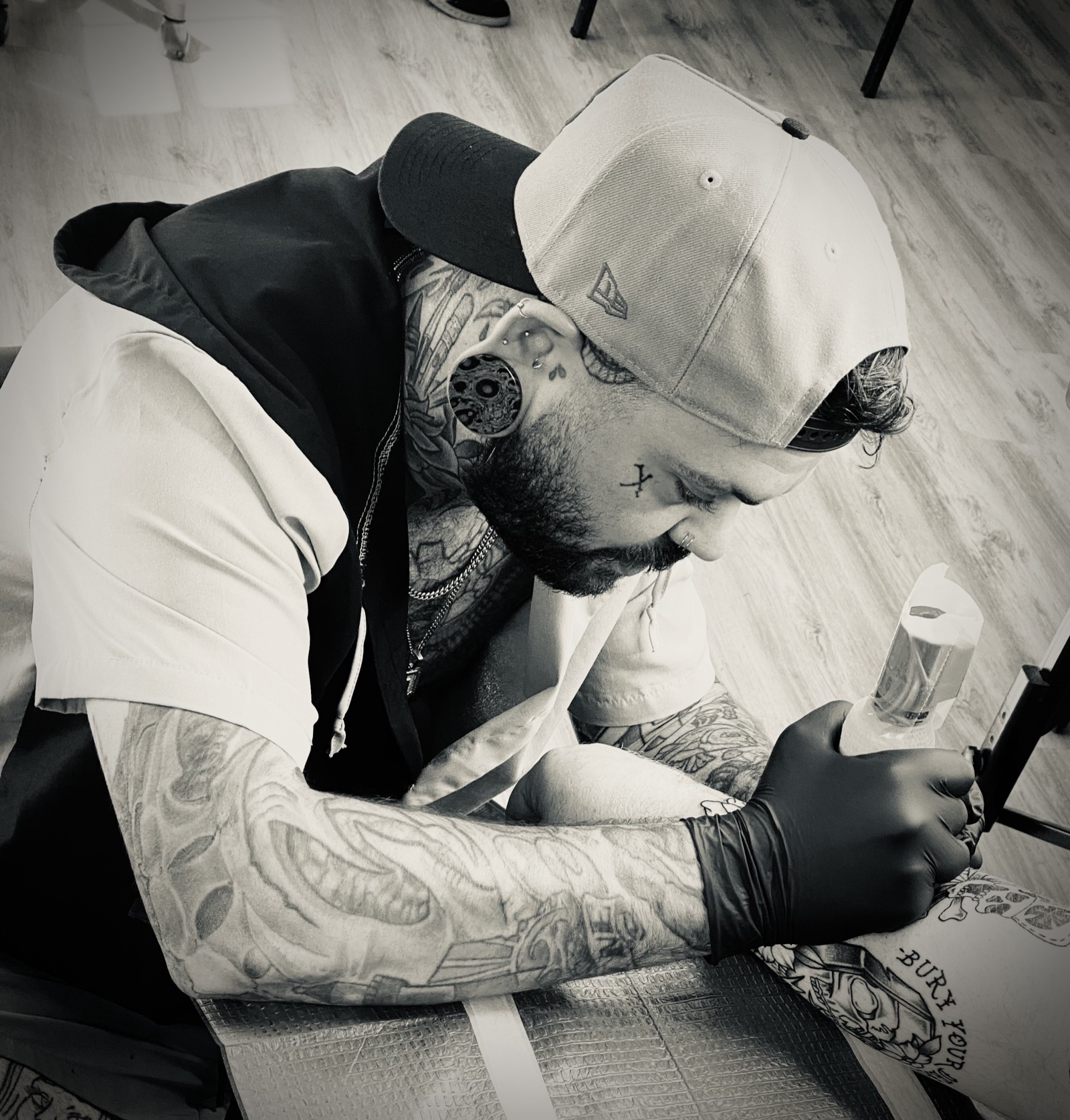 Artist tattooing a client's arm, focused, in black and white