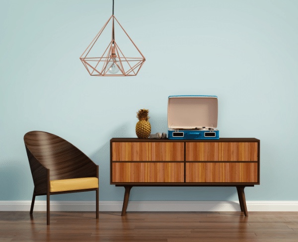 A walnut mid-century credenza with a turntable beneath a copper geometric pendant, paired with a sculptural walnut chair against a pale-blue wall