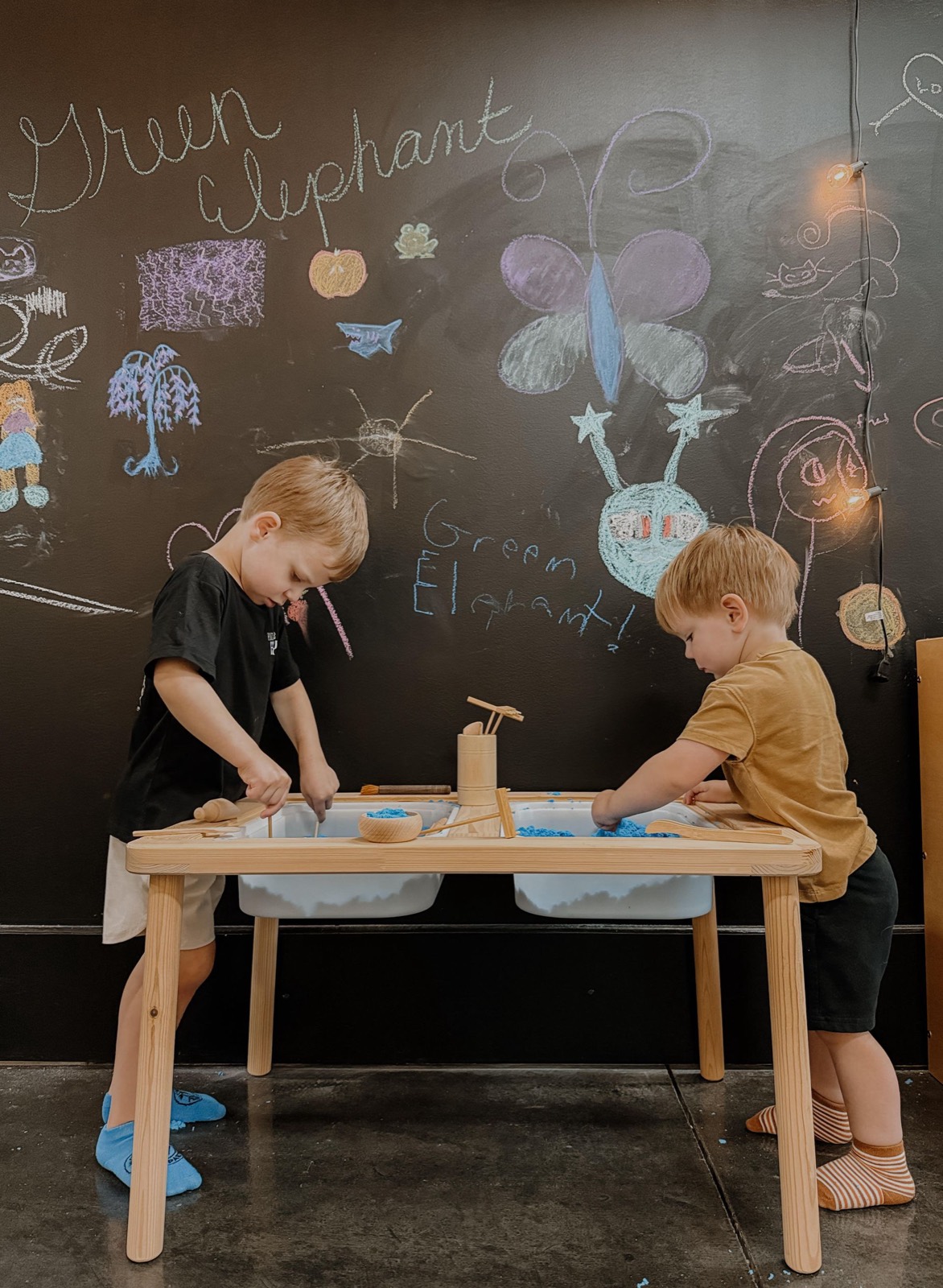 Two children playing at a sensory table in front of the Green Elephant chalkboard wall
